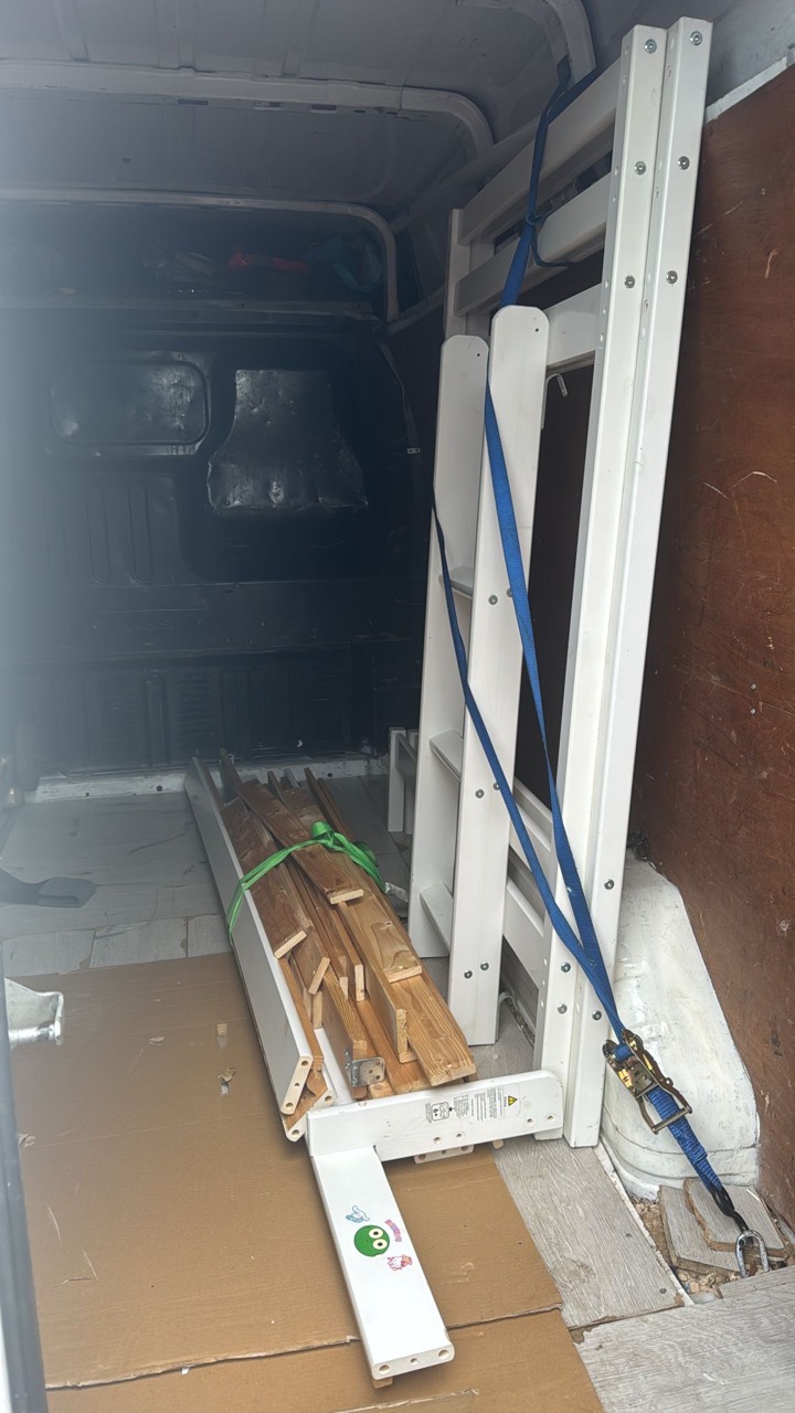 Dismantled bed frame secured upright inside a van with ratchet straps