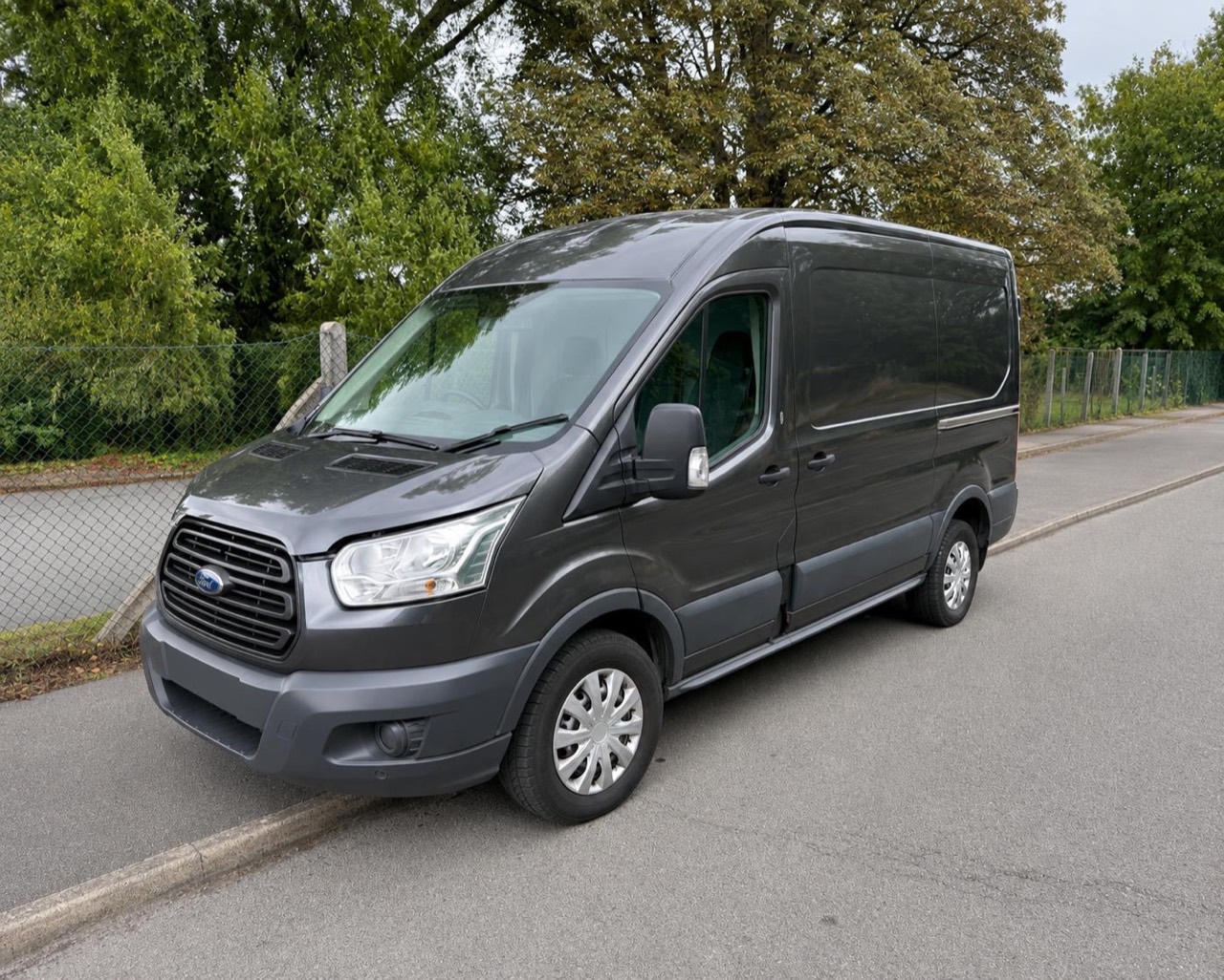 A dark grey Ford Transit van parked on a residential road